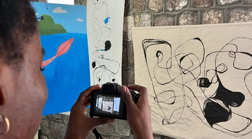 An artist photographing paintings on display at the Bloom Where You're Planted exhibition